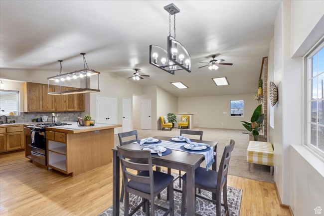 Dining space with ceiling fan with notable chandelier, light wood-style floors, and vaulted ceiling | Image 5