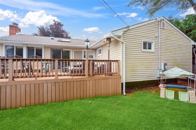 Rear view of property featuring a lawn, a wooden deck, a chimney, and a shingled roof | Image 23