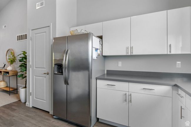 Kitchen with stainless steel fridge with ice dispenser, white cabinets, visible vents, and wood finished floors | Image 17