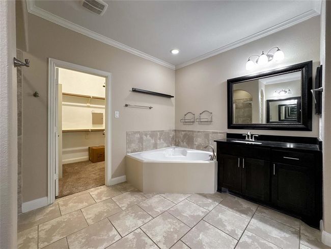 This bathroom features a corner soaking tub, a sleek vanity with a large framed mirror, and tiled flooring. It also includes a spacious walk-in closet for ample storage. | Image 40