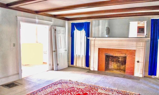 Unfurnished living room with carpet floors, a fireplace with flush hearth, and beamed ceiling | Image 12