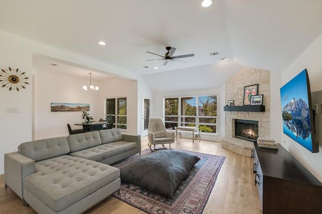 Living room featuring a ceiling fan, light wood-style floors, a fireplace, a chandelier, and vaulted ceiling | Image 4