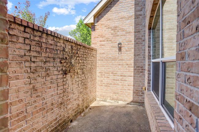 This is a side patio, accessible via the study, features a tall privacy brick wall and the side of a brick home with large windows, potentially offering a private outdoor space with a decorative touch. | Image 28