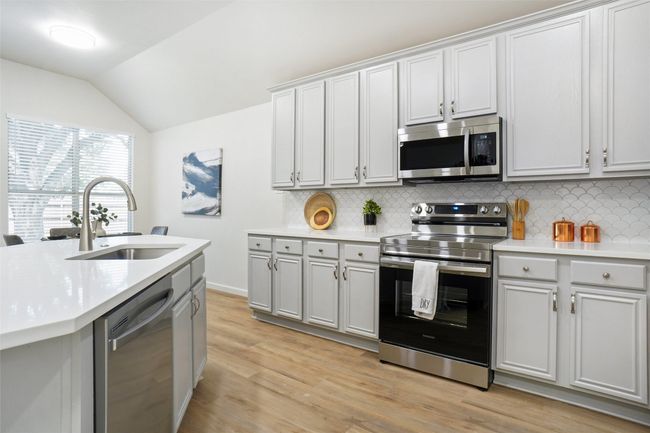 Kitchen with appliances with stainless steel finishes, a sink, vaulted ceiling, tasteful backsplash, and light countertops | Image 6