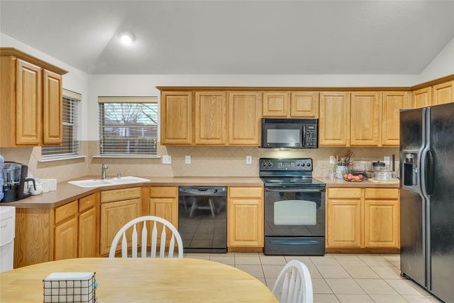 Kitchen featuring black appliances, vaulted ceiling, light tile patterned floors, light countertops, and decorative backsplash | Image 14