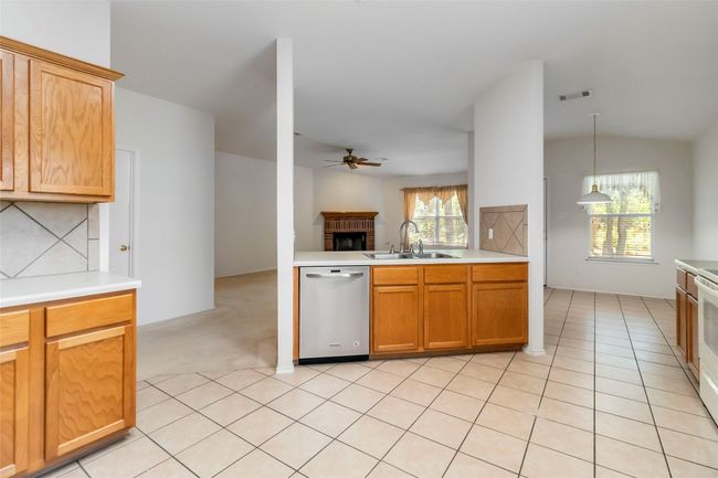 Kitchen with dishwasher, a sink, a ceiling fan, a brick fireplace, and light countertops | Image 15