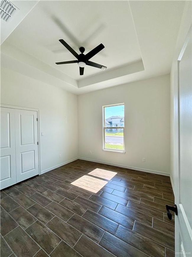 Empty room with a tray ceiling, baseboards, wood finish floors, and a ceiling fan | Image 11