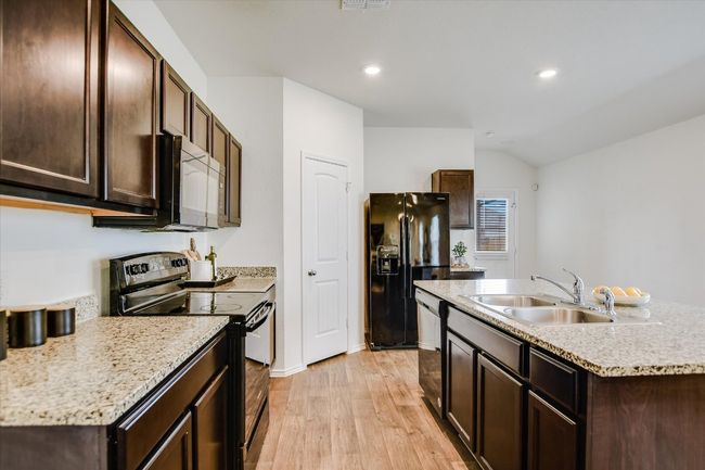 Kitchen featuring dark brown cabinets, light countertops, a sink, light wood finished floors, and black appliances | Image 8
