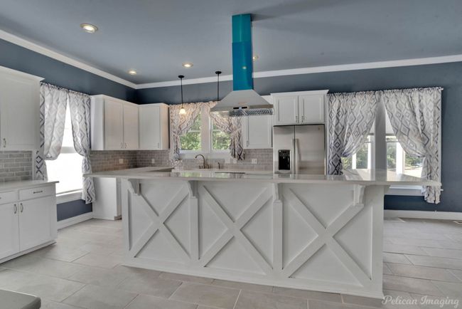 Kitchen featuring island exhaust hood, stainless steel fridge with ice dispenser, light countertops, decorative backsplash, and recessed lighting | Image 5