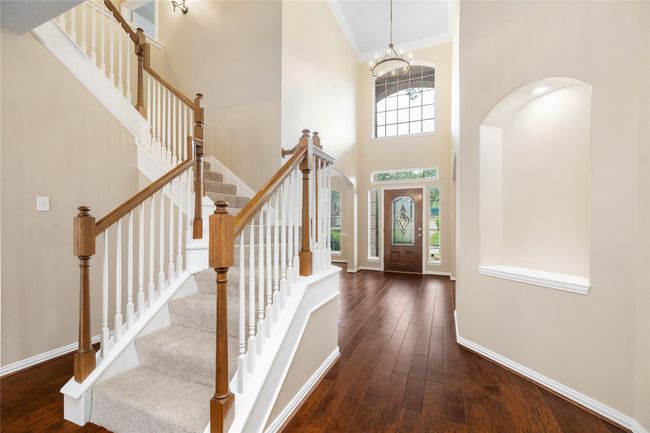 Showcasing a bright and welcoming foyer, this entry features high ceilings, a large window above the front door, and a wooden staircase with white spindles. | Image 25