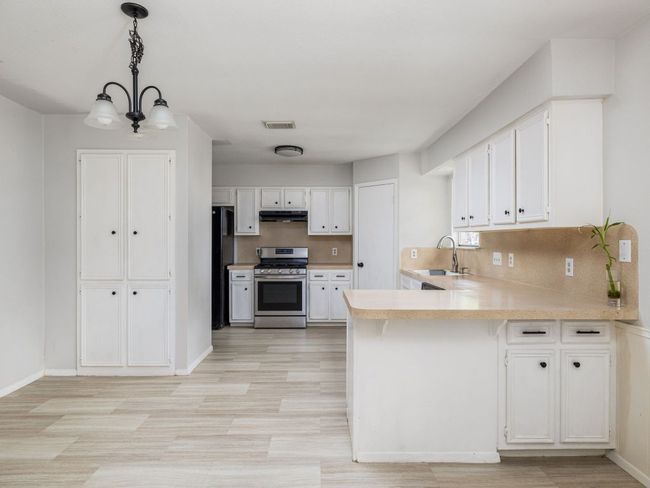 Kitchen with gas stove, under cabinet range hood, a peninsula, light countertops, and white cabinetry | Image 7
