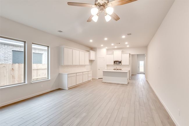 Kitchen with stainless steel microwave, ceiling fan, decorative backsplash, a kitchen island with sink, and white cabinetry | Image 6