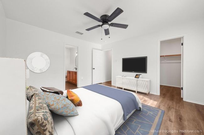 Virtually staged Primary Bedroom with visible vents, baseboards, ceiling fan, wood finished floors, and a walk in closet | Image 10