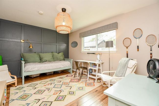 This cozy room features a dark accent wall with a daybed, stylish lighting, and a desk area by a large window. It has a warm wood floor, colorful area rug, and vintage tennis rackets as decor, creating a charming and inviting space. | Image 31