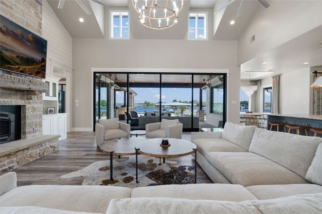 Living room with high vaulted ceiling, a chandelier, wood finished floors, and a fireplace | Image 7