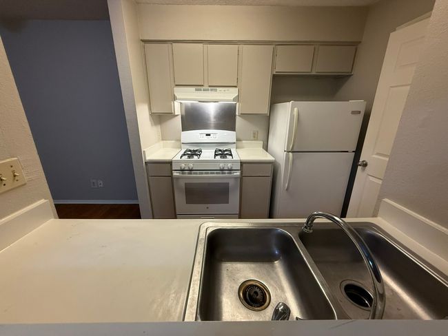Kitchen featuring white appliances, under cabinet range hood, light countertops, and dark wood finished floors | Image 6