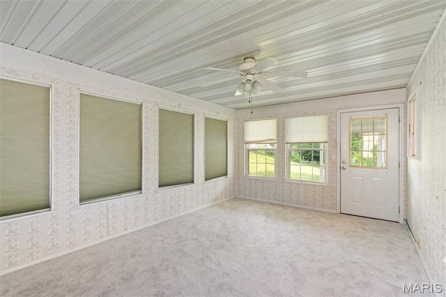 Unfurnished sunroom featuring wallpapered walls, ceiling fan, plenty of natural light, and carpet flooring | Image 10