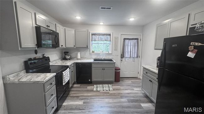 Kitchen with black appliances, a sink, gray cabinets, light countertops, and wood finished floors | Image 5