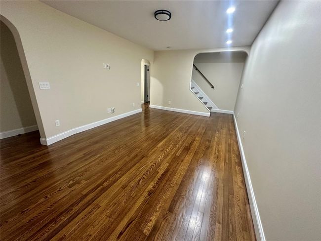 Unfurnished living room featuring baseboards, arched walkways, stairs, and dark wood-style flooring | Image 4
