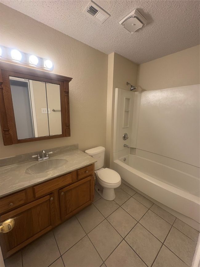 Bathroom featuring toilet, vanity, a textured ceiling, tile patterned flooring, and visible vents | Image 15