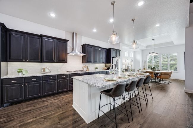 Kitchen with wall chimney range hood, a tray ceiling, dark wood finished floors, a breakfast bar, and a kitchen island with sink | Image 8