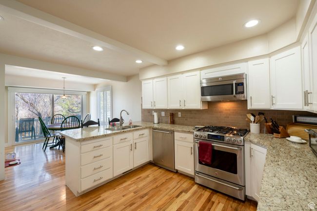 Kitchen featuring a sink, light wood-type flooring, a peninsula, white cabinetry, and stainless steel appliances | Image 21