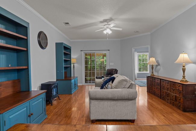 Living room featuring a wood stove, a ceiling fan, wood finished floors, and crown molding | Image 16