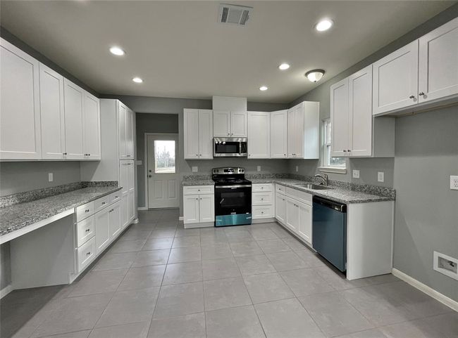 This kitchen features modern white soft close cabinetry, granite countertops, and sleek tile flooring. | Image 5