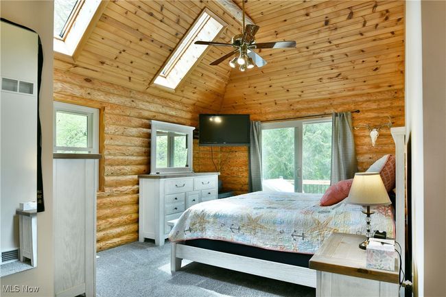 Carpeted bedroom featuring a skylight, multiple windows, rustic walls, high vaulted ceiling, and wood ceiling | Image 24
