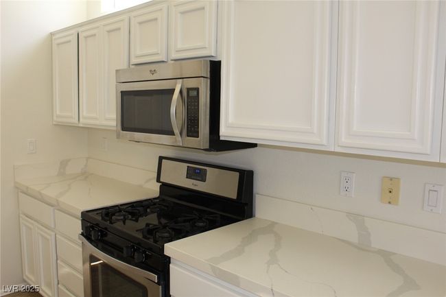 Kitchen with light stone countertops, appliances with stainless steel finishes, and white cabinetry | Image 11