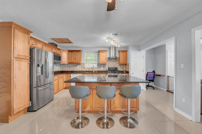 Kitchen with wall chimney range hood, a sink, stainless steel appliances, tasteful backsplash, and visible vents | Image 23