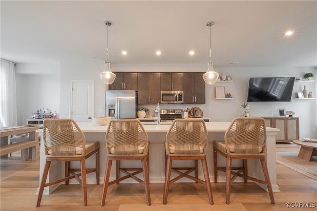 Kitchen featuring dark brown cabinets, light wood-type flooring, stainless steel appliances, a center island with sink, and light countertops | Image 7