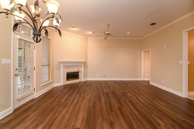 living room with wood floors, a chandelier, ornamental molding, a ceiling fan, and baseboards | Image 4