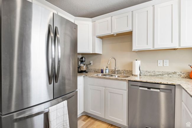 Kitchen featuring light wood-type flooring, white cabinets, light stone counters, a sink, and stainless steel appliances | Image 14