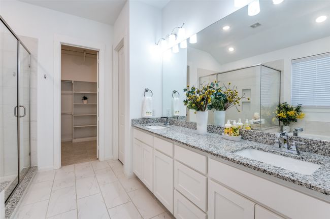 Luxurious master ensuite featuring elegant tile flooring, a dual-sink vanity with a granite countertop, a spacious walk-in closet, a relaxing Texas tub, and a separate walk-in shower. | Image 18