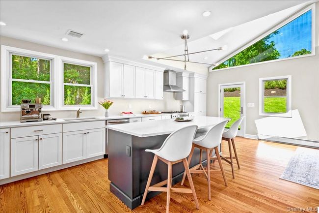 Kitchen featuring a sink, wall chimney exhaust hood, light wood floors a kitchen bar, and light countertops | Image 11