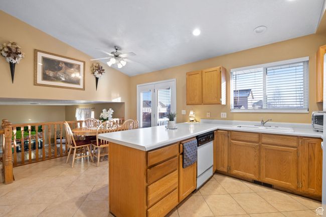 Kitchen with vaulted ceiling, light tile patterned flooring, sink, white dishwasher, and kitchen peninsula | Image 10