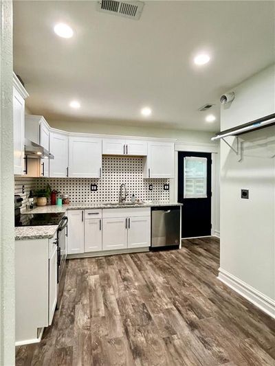 Kitchen with wall chimney range hood, dark hardwood / wood-style flooring, white cabinetry, stainless steel appliances, and decorative backsplash | Image 3