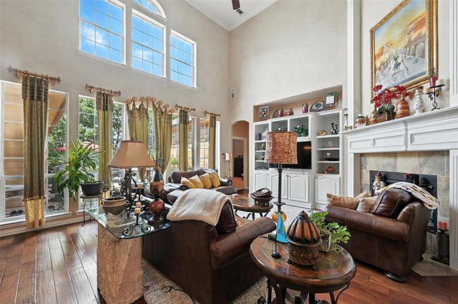 Living area with a towering ceiling, ornamental molding, hardwood / wood-style floors, arched walkways, and a tile fireplace | Image 11