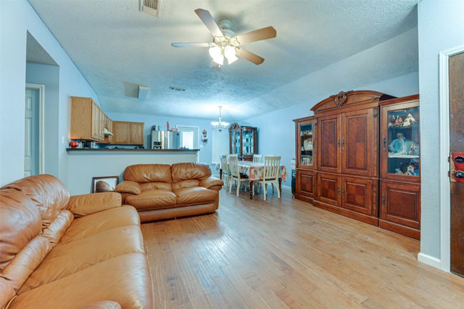 Living area with a textured ceiling, ceiling fan with notable chandelier, light wood finished floors, baseboards, and visible vents | Image 15
