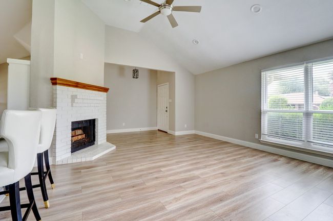 Unfurnished living room featuring ceiling fan, lofted ceiling, a fireplace, and light wood-type flooring | Image 6