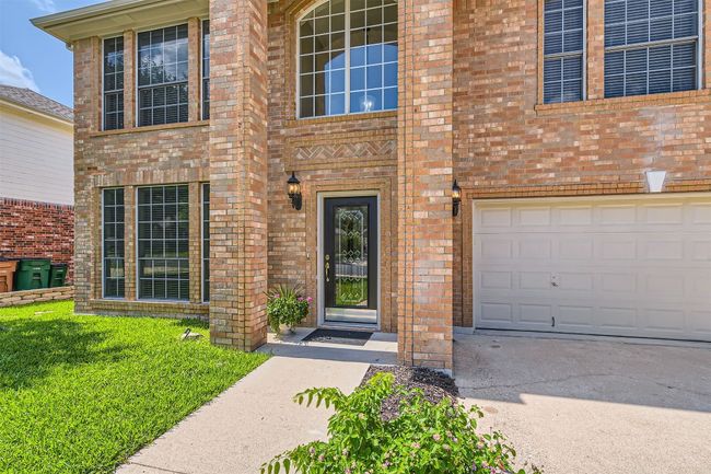 View of exterior entry with an attached garage, brick siding, concrete driveway, and a yard | Image 5