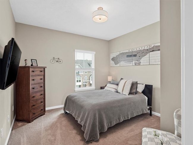 This comfortable secondary bedroom offers a cozy and inviting atmosphere with neutral-toned walls and plush carpeting. A large window allows natural light to brighten the space, while the room's layout easily accommodates a full-sized bed and additional furniture. Stylish yet functional, this room is perfect for guests, family members, or a home office. Thoughtful details, including a wall-mounted TV and tasteful decor, complete the look of this well-appointed space. | Image 20