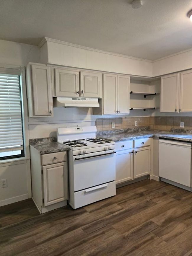 Kitchen with white appliances, under cabinet range hood, open shelves, and dark wood-style flooring | Image 8
