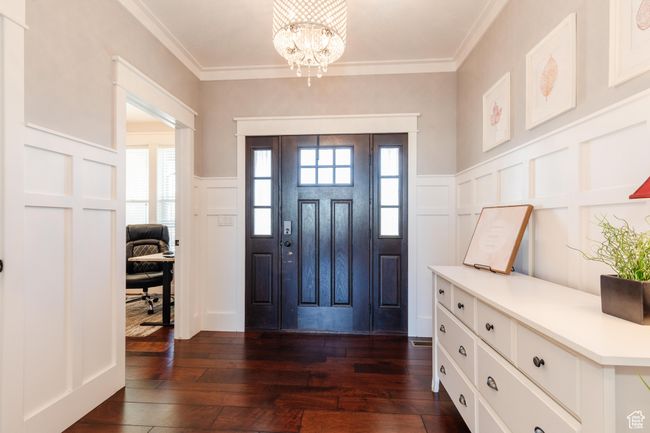 Foyer entrance featuring a decorative wall, dark wood-type flooring, a chandelier, wainscoting, and ornamental molding | Image 4