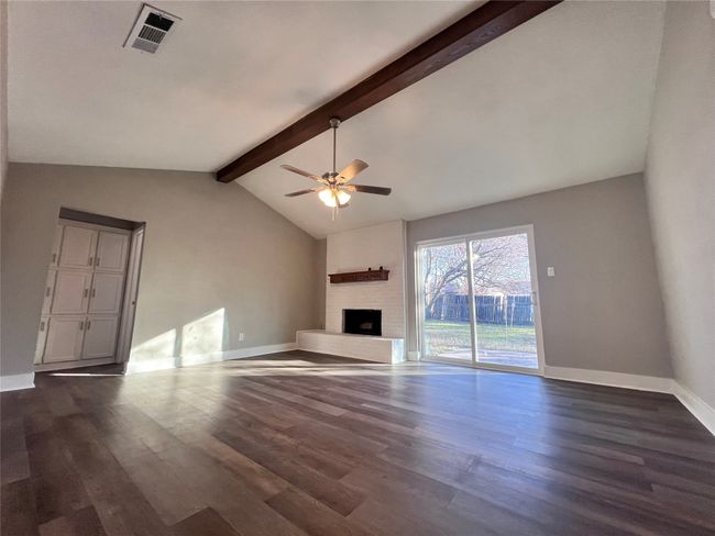 Unfurnished living room featuring ceiling fan, dark hardwood / wood-style flooring, a fireplace, and vaulted ceiling with beams | Image 11