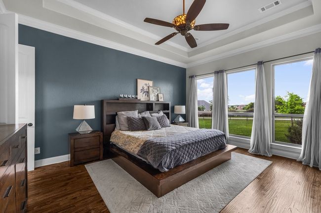 Bedroom with a raised ceiling, dark wood-style floors, crown molding, baseboards, and ceiling fan | Image 12