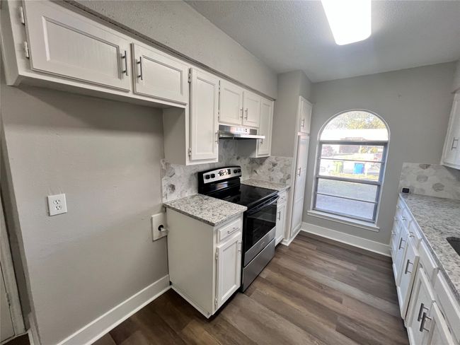 Kitchen with light stone countertops, white cabinets, tasteful backsplash, dark hardwood / wood-style floors, and stainless steel electric range | Image 8