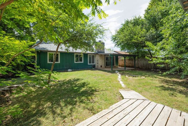 Rear view of property featuring board and batten siding, a chimney, a deck, a patio, and a carport | Image 21