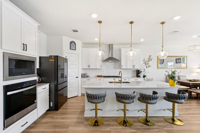 Kitchen featuring wall chimney range hood, stainless steel appliances, light countertops, a kitchen bar, and recessed lighting | Image 10